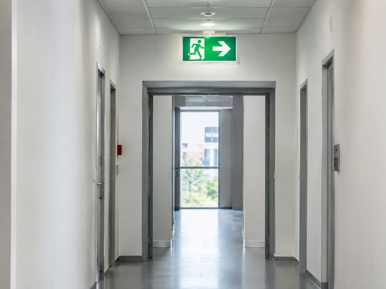 Couloir de bâtiment tertiaire avec panneau lumineux indiquant la sortie de secours